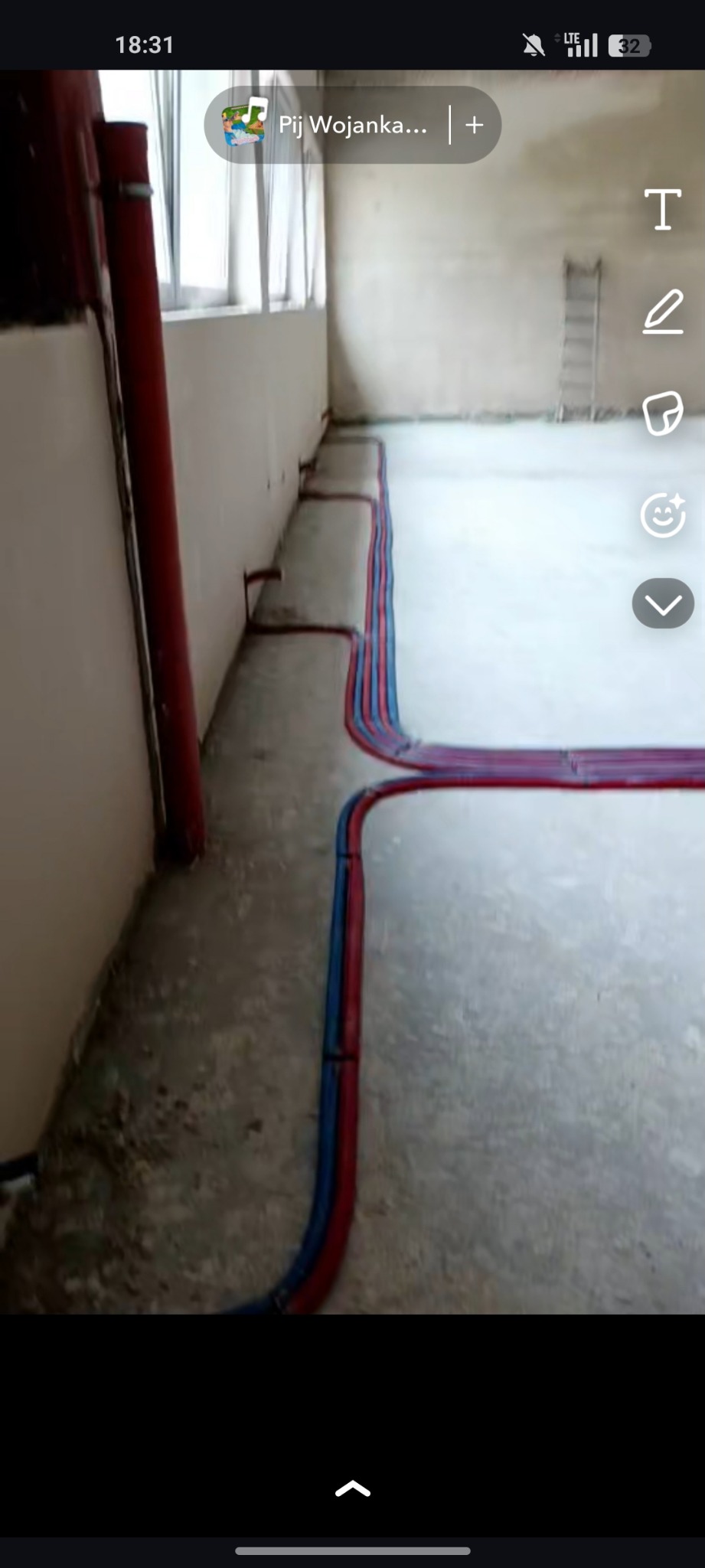 Ułożone rury instalacji hydraulicznej (czerwone i niebieskie) na podłodze w surowym pomieszczeniu. Widoczna drabina w tle.