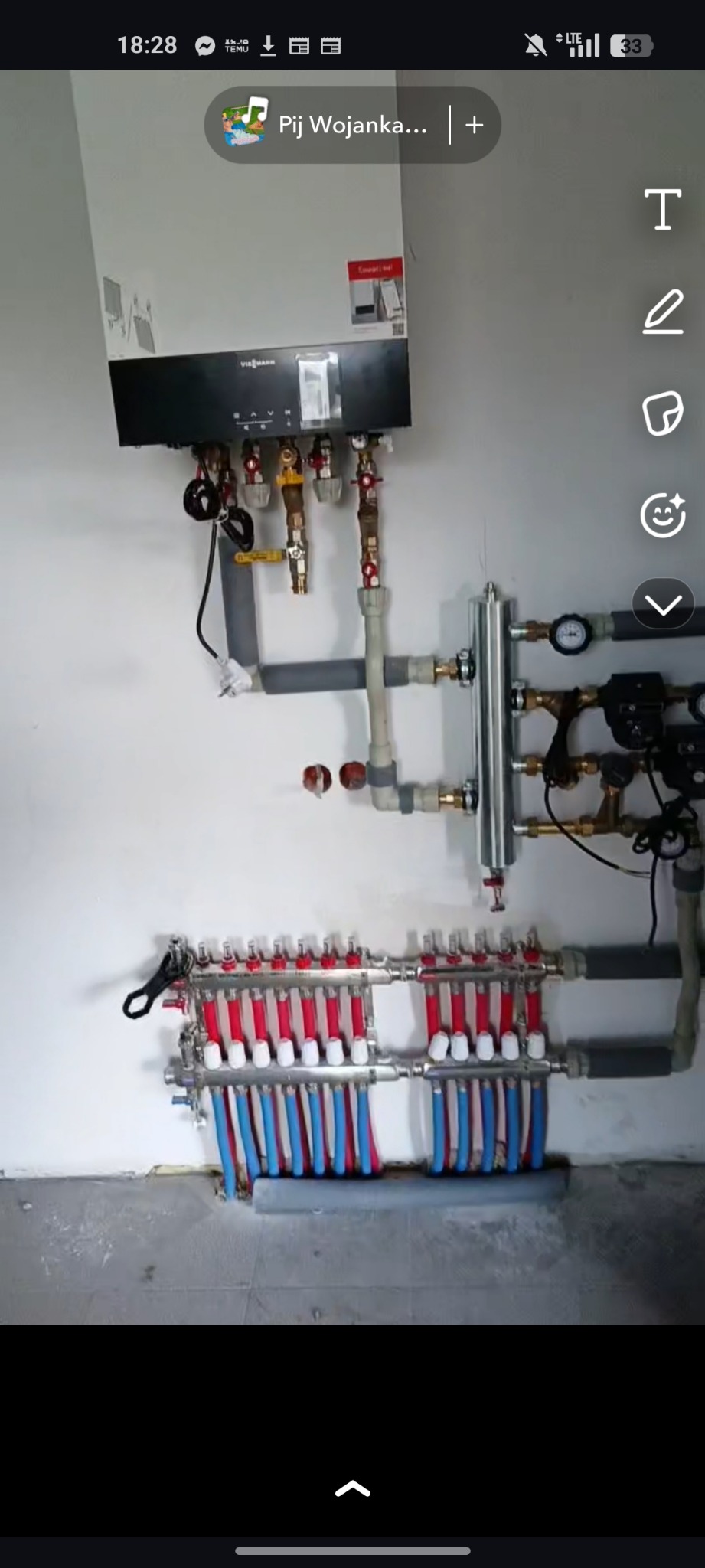 Rozdzielacz ogrzewania podłogowego z kotłem Viessmann na ścianie. Widoczne rury w kolorach czerwonym i niebieskim. Instalacja grzewcza w kotłowni.