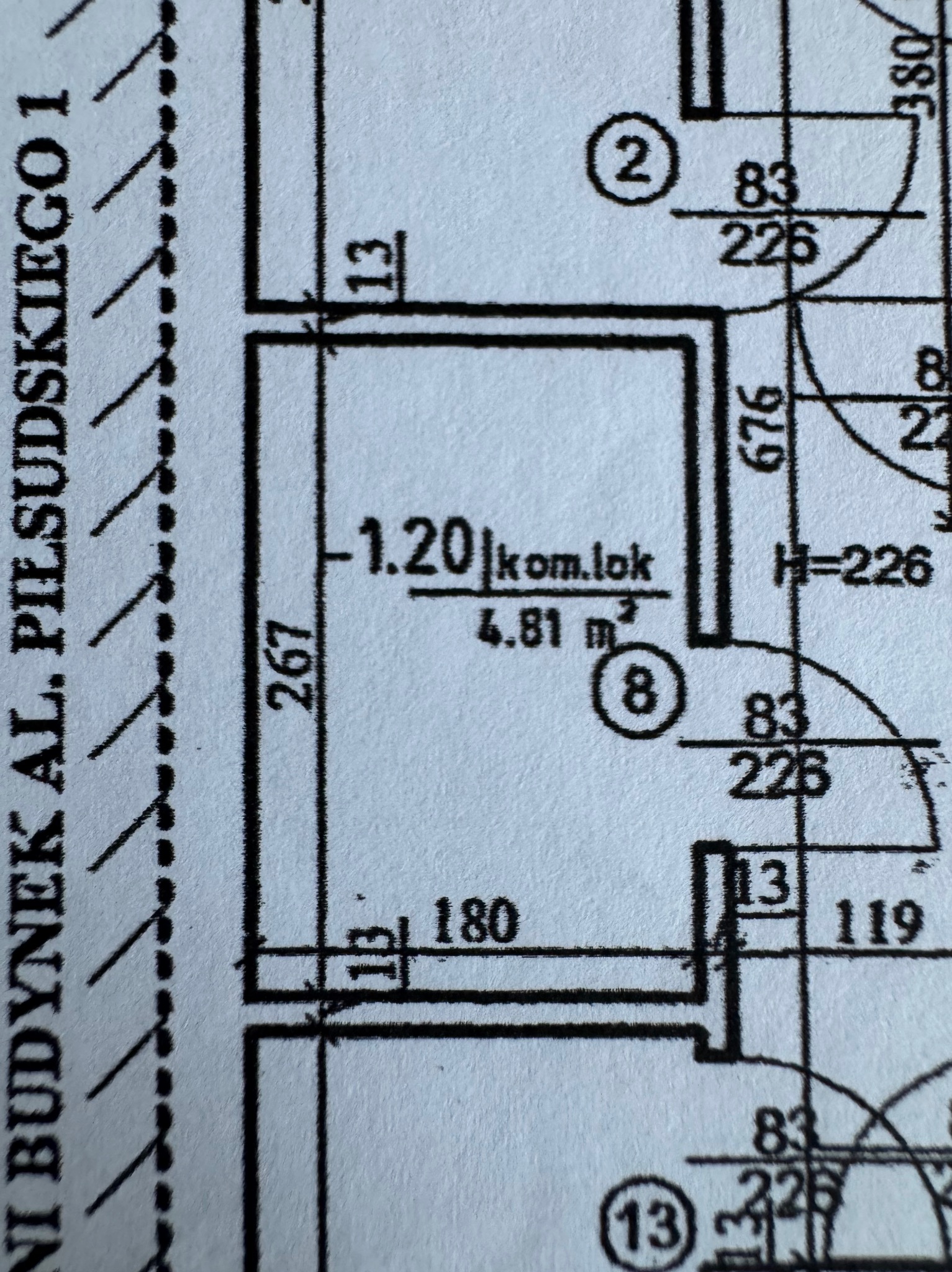 Fragment planu mieszkania z wymiarami i oznaczeniami pomieszczeń, widoczny adres budynku Al. Piłsudskiego 1. Czarno-biały rysunek techniczny.
