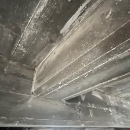 Ziolopol - Szare, surowe żelbetowe belki stropowe z widocznym deskowaniem, sfotografowane pod kątem od dołu, ukazujące strukturę betonu i drewniane odciski.