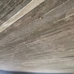 Ziolopol - Betonowy strop z odciskiem desek szalunkowych, widoczny pod kątem. Szara powierzchnia z wyraźnym rysunkiem drewna i śladami po szalunku.