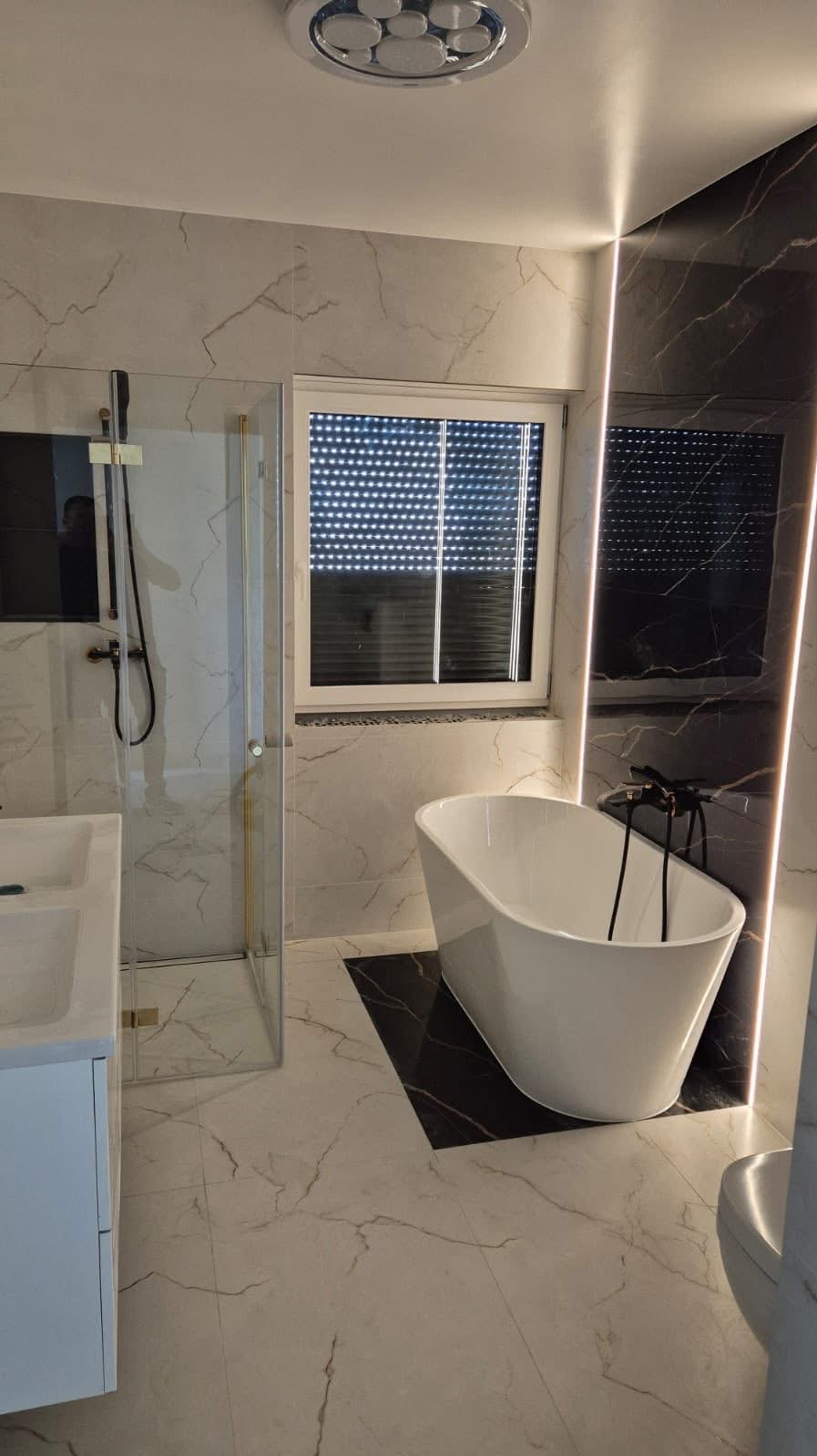 Nowoczesna łazienka z marmurowymi płytkami, wolnostojącą wanną i kabiną prysznicową ze złotymi akcentami. Oświetlenie LED podkreśla elegancki design.