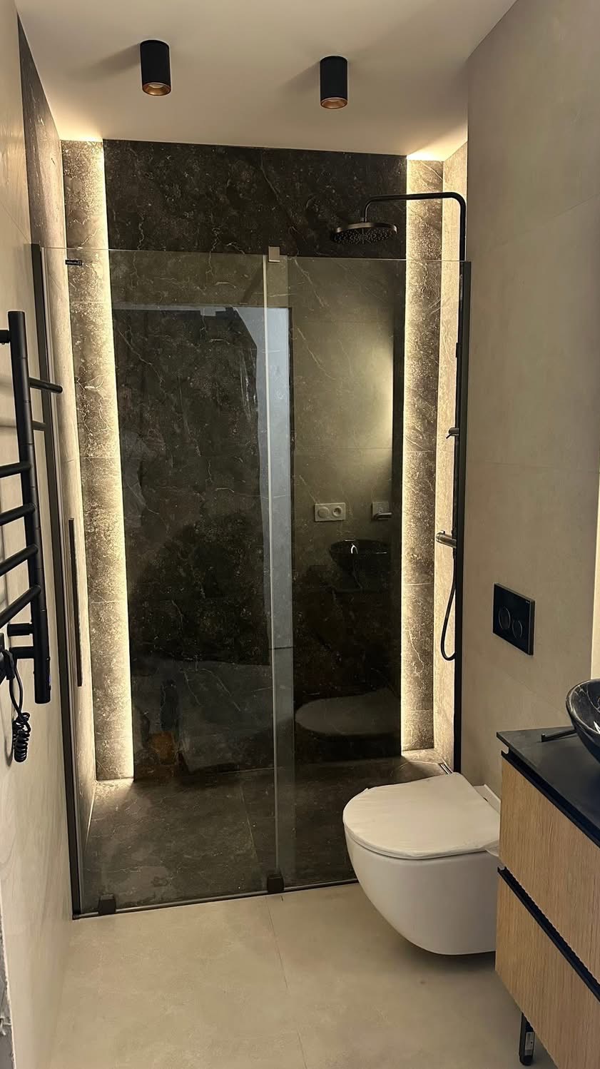 Nowoczesna łazienka z kabiną prysznicową typu walk-in, podświetleniem LED i czarną armaturą. Uwagę zwraca marmurowa ściana w kabinie i minimalistyczna toaleta.