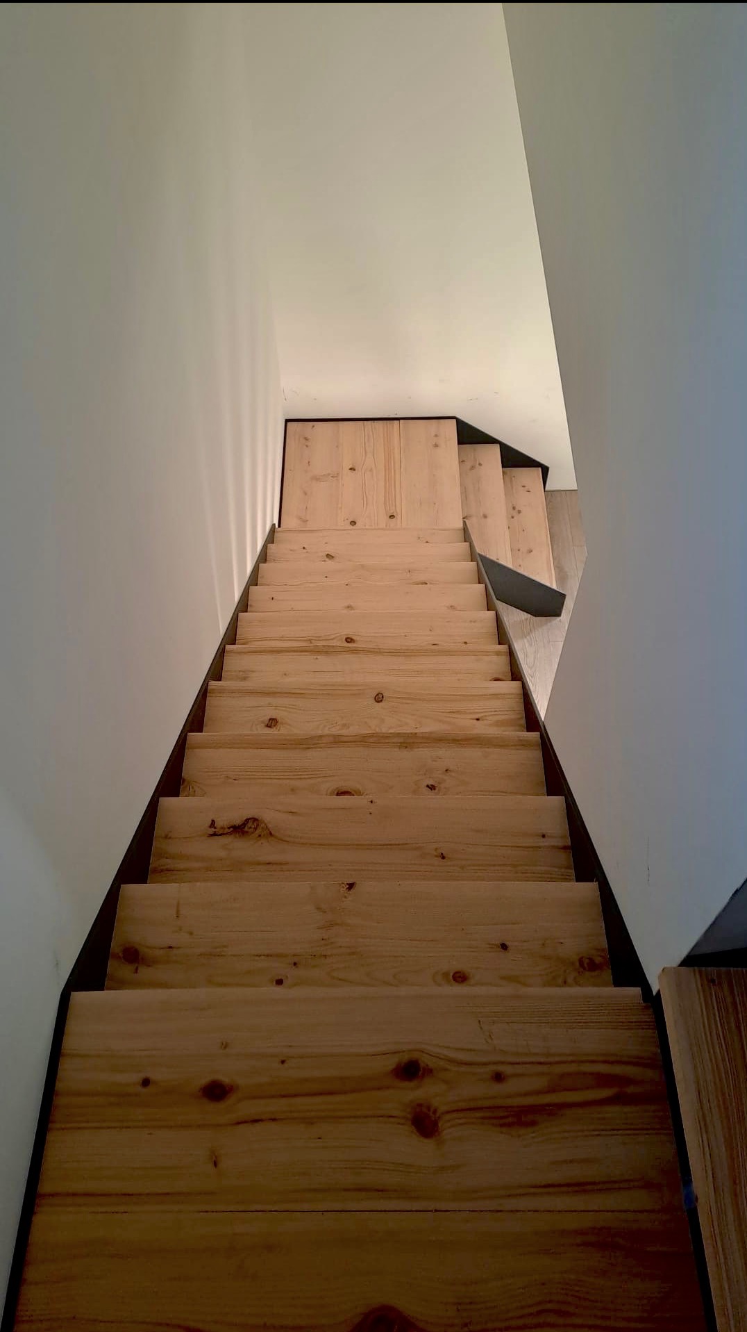 Drewniane schody z ciemnymi krawędziami, widok z góry, ukazujące naturalne usłojenie drewna i minimalistyczny design w jasnym wnętrzu.