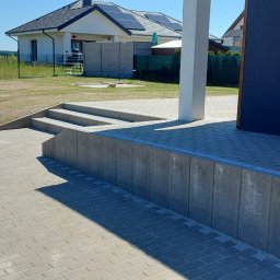 WichBUD Piotr Nochowicz - Jasnoszara kostka brukowa ułożona przed nowoczesnym domem z panelami słonecznymi. Widoczne schody wejściowe i fragment elewacji w kolorze granatowym.