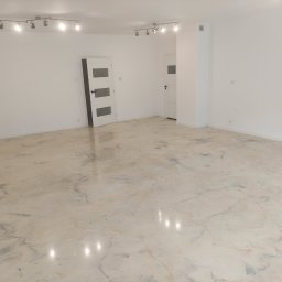 WichBUD Piotr Nochowicz - Jasne wnętrze z posadzką żywiczną imitującą marmur, widoczne białe drzwi i oświetlenie sufitowe. Minimalistyczny design, gładka powierzchnia podłogi.