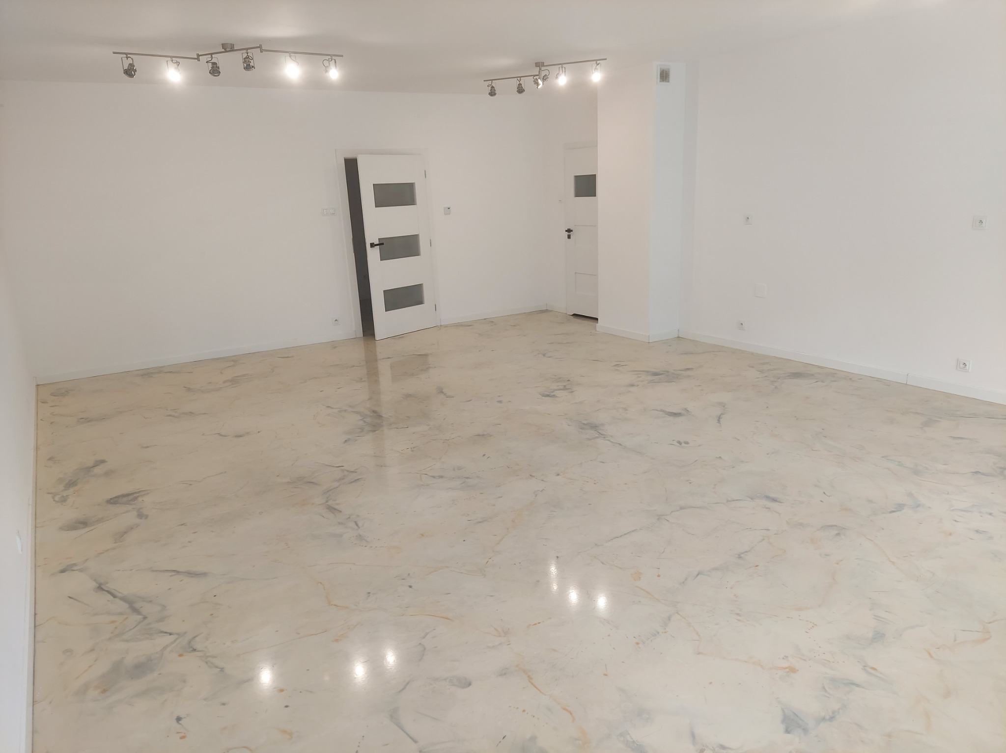 Jasne wnętrze z posadzką żywiczną imitującą marmur, widoczne białe drzwi i oświetlenie sufitowe. Minimalistyczny design, gładka powierzchnia podłogi.