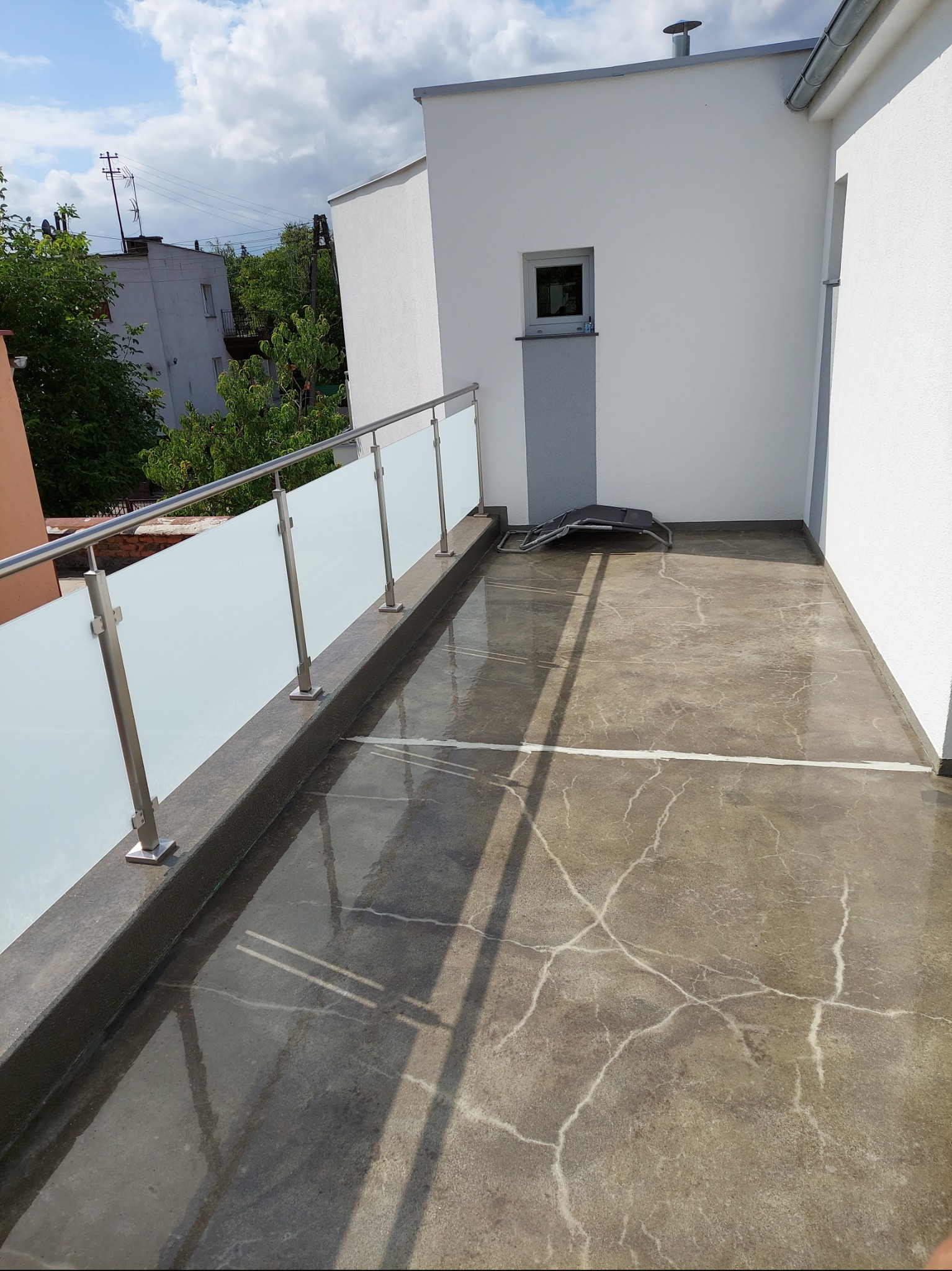 Balkon z posadzką żywiczną w Obornikach, wykończony szklaną balustradą i metalowymi elementami. Widoczne refleksy światła na gładkiej powierzchni posadzki.
