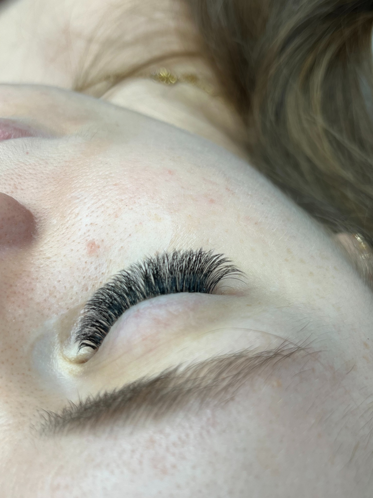 Zbliżenie na oko kobiety z gęstymi, czarnymi, sztucznymi rzęsami. Widoczna delikatna skóra powiek i fragment brwi. Makro detale podkreślają precyzję aplikacji.
