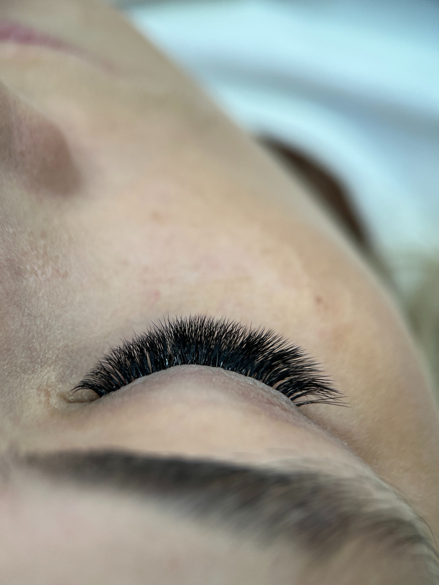 Zbliżenie na oko z gęstymi, czarnymi, profesjonalnie przedłużonymi rzęsami. Widoczna delikatna skóra powiek i brwi. Efekt stylizacji rzęs.