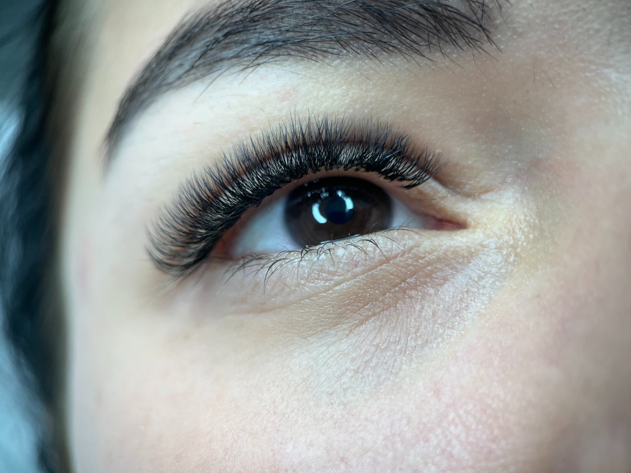 Zbliżenie na oko z gęstymi, czarnymi rzęsami po zabiegu przedłużania. Widoczna precyzja aplikacji i naturalny efekt. Makro, ostre światło.