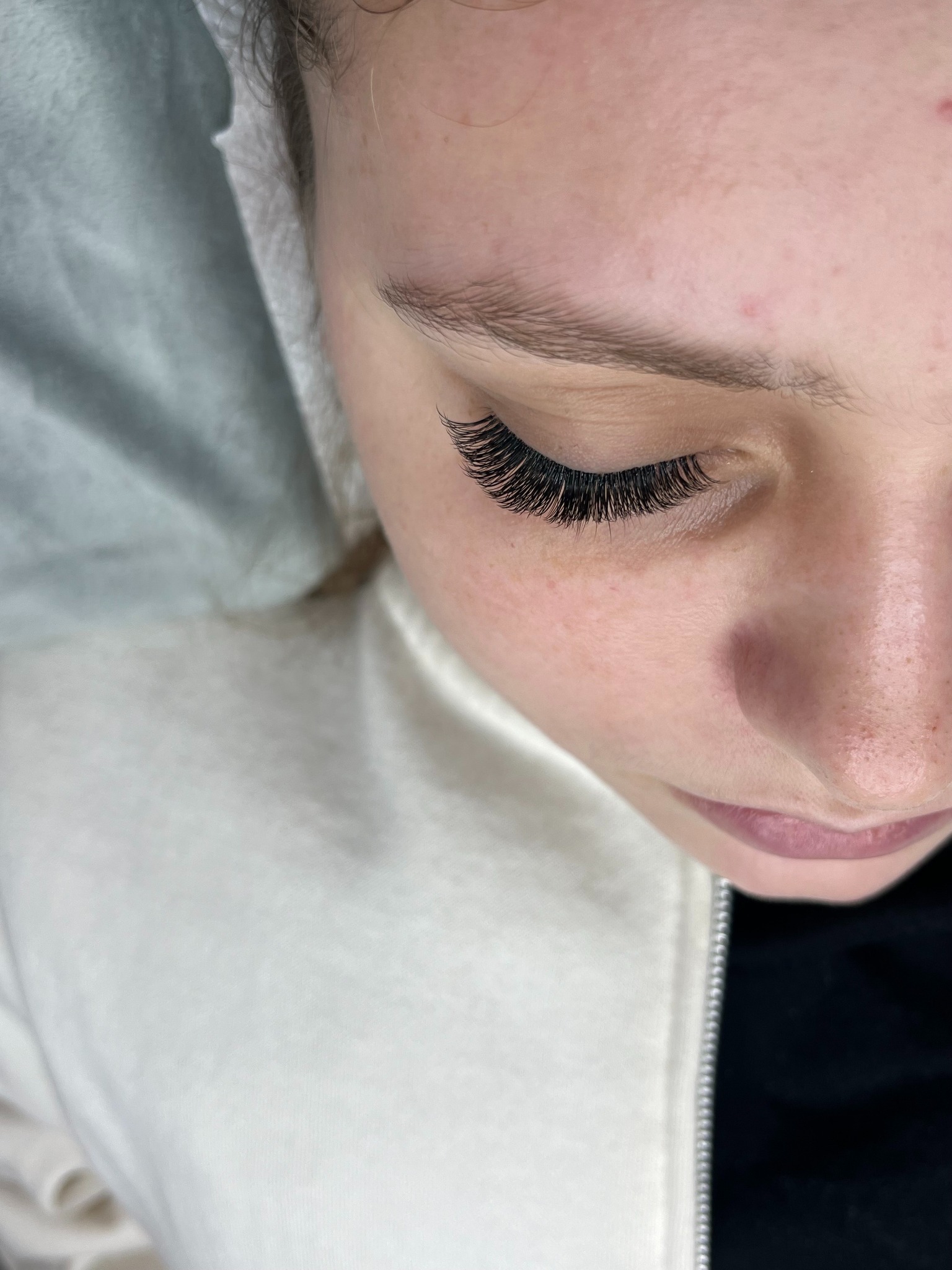 Zbliżenie na oko kobiety po zabiegu przedłużania rzęs. Widoczne długie, gęste, czarne rzęsy. Delikatny makijaż ust. Ujęcie z góry, oświetlenie studyjne.