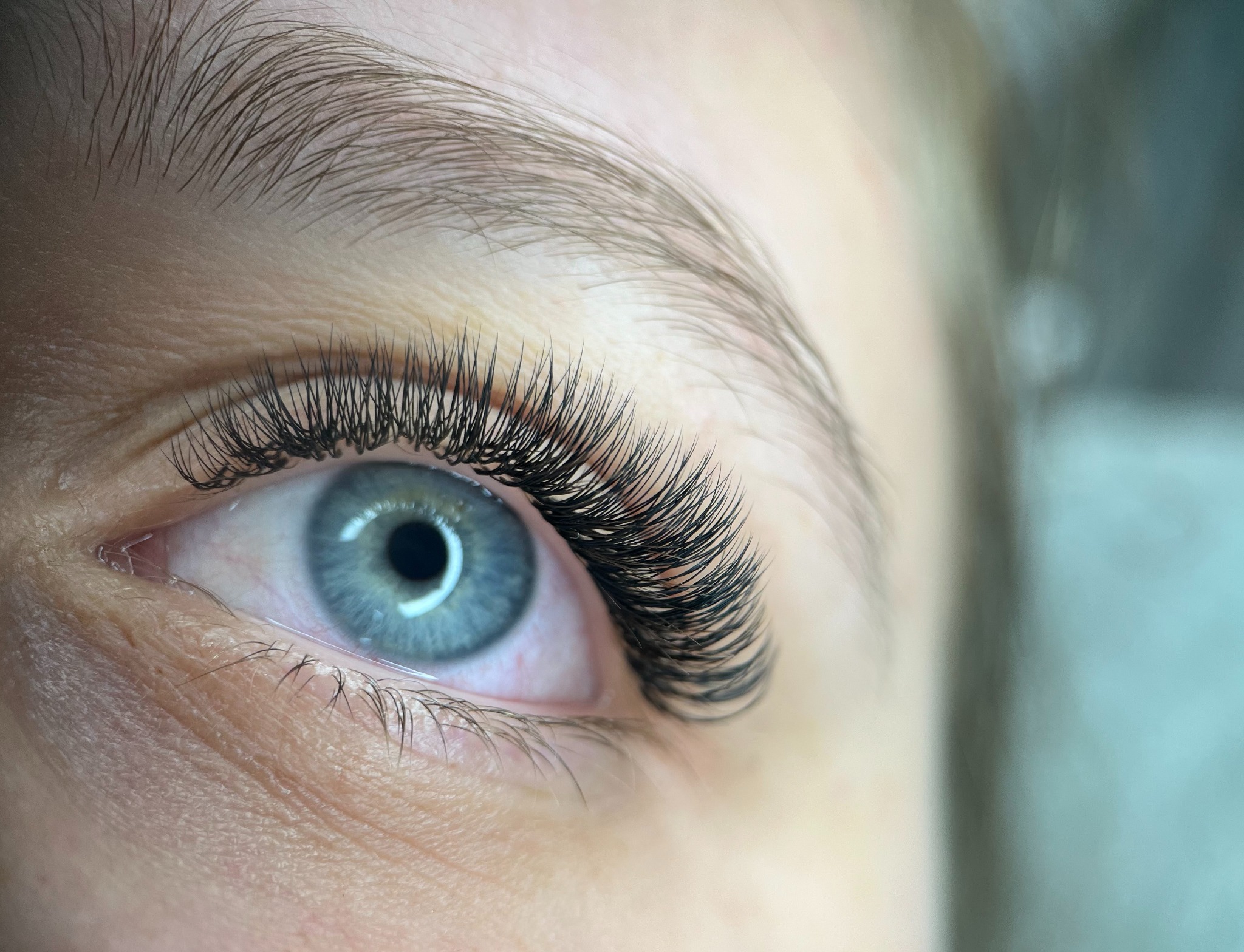 Zbliżenie na oko z gęstymi, profesjonalnie przedłużonymi rzęsami. Błękitna tęczówka i naturalny kształt brwi podkreślają efekt zabiegu upiększającego.