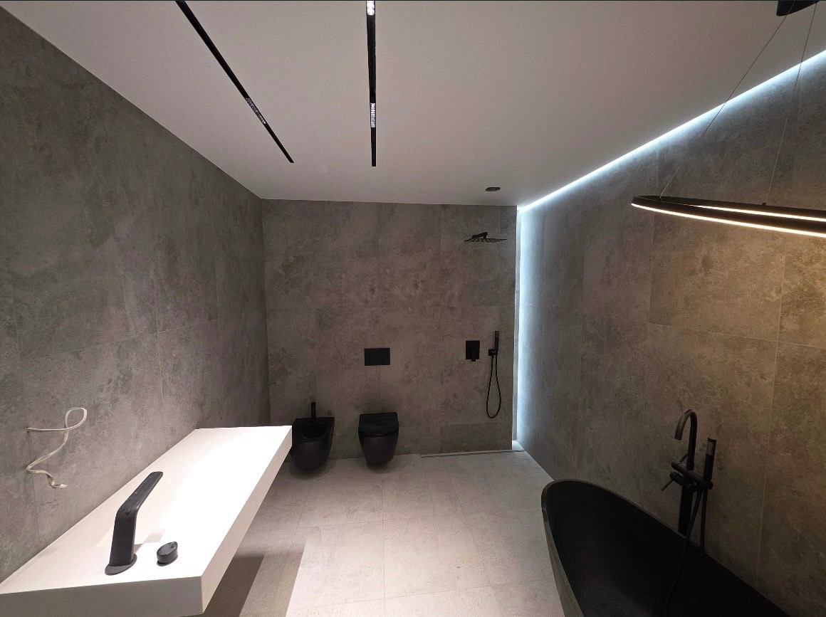 Nowoczesna łazienka w szarościach z czarną armaturą i podświetleniem LED. Minimalistyczny design z wanną wolnostojącą i podwieszaną toaletą.