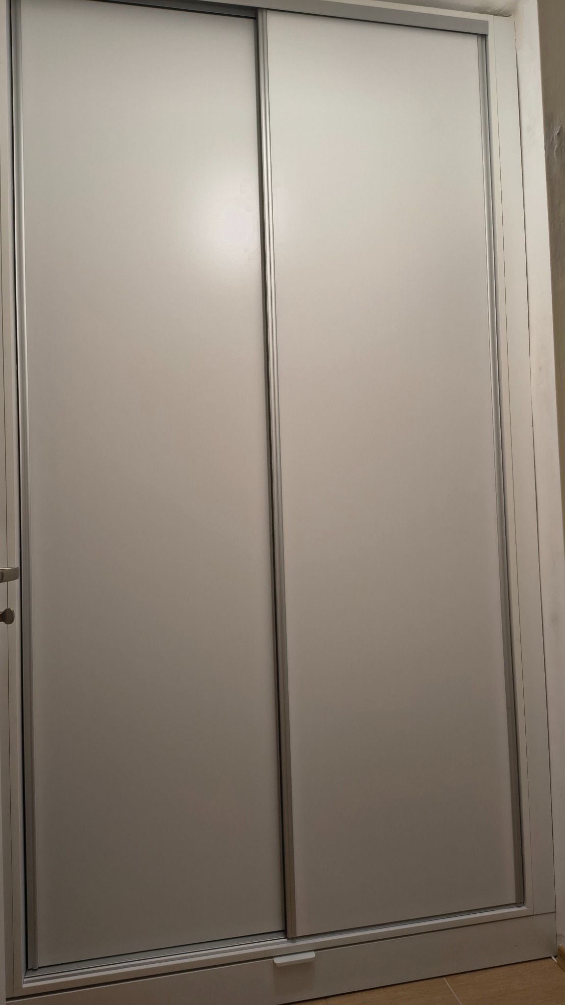 Minimalistyczna szafa wnękowa z przesuwnymi drzwiami w odcieniach bieli i szarości, zrealizowana w Zawoi. Proste linie, nowoczesny design.