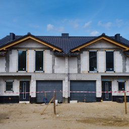 VIS - Dwukondygnacyjny bliźniak w stanie surowym zamkniętym z ciemną dachówką, widoczne okna i drzwi, teren budowy zabezpieczony taśmą ostrzegawczą.