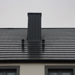 VIS - Grafitowy dach z ceramicznej dachówki karpiówki, z kominem i odpowietrznikami, widziany z dołu na tle pochmurnego nieba. Nowoczesne wykończenie.