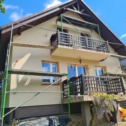 Ecoenergy 4 You - Dwupiętrowy dom w trakcie prac elewacyjnych, z rusztowaniem i widocznym balkonem z drewnianą balustradą. Świeżo otynkowana fasada w odcieniach beżu i brązu.