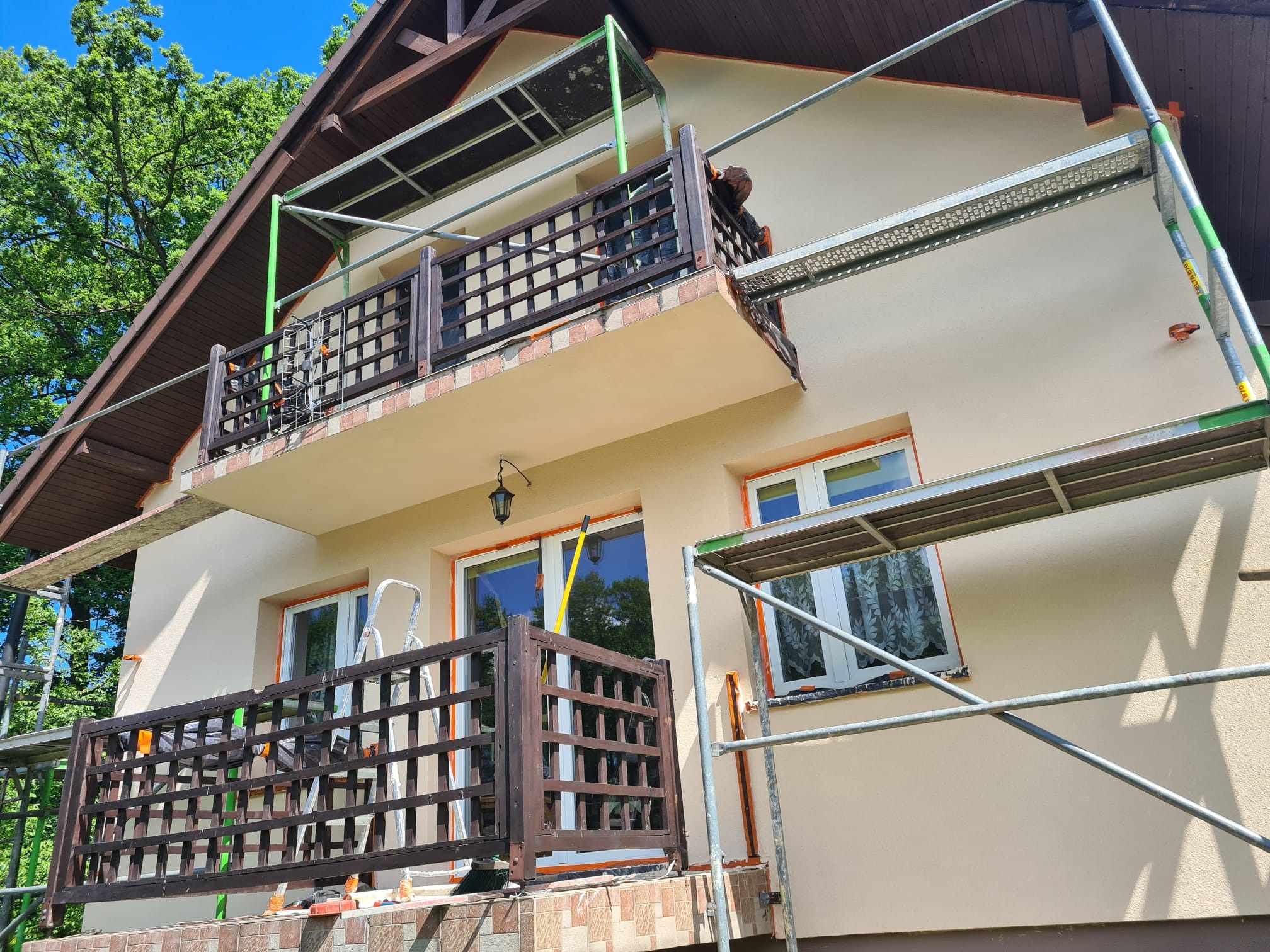 Dom z balkonami w Żorach w trakcie prac elewacyjnych. Widoczne rusztowania i świeżo nałożony tynk w odcieniach beżu. Prace na wysokości.