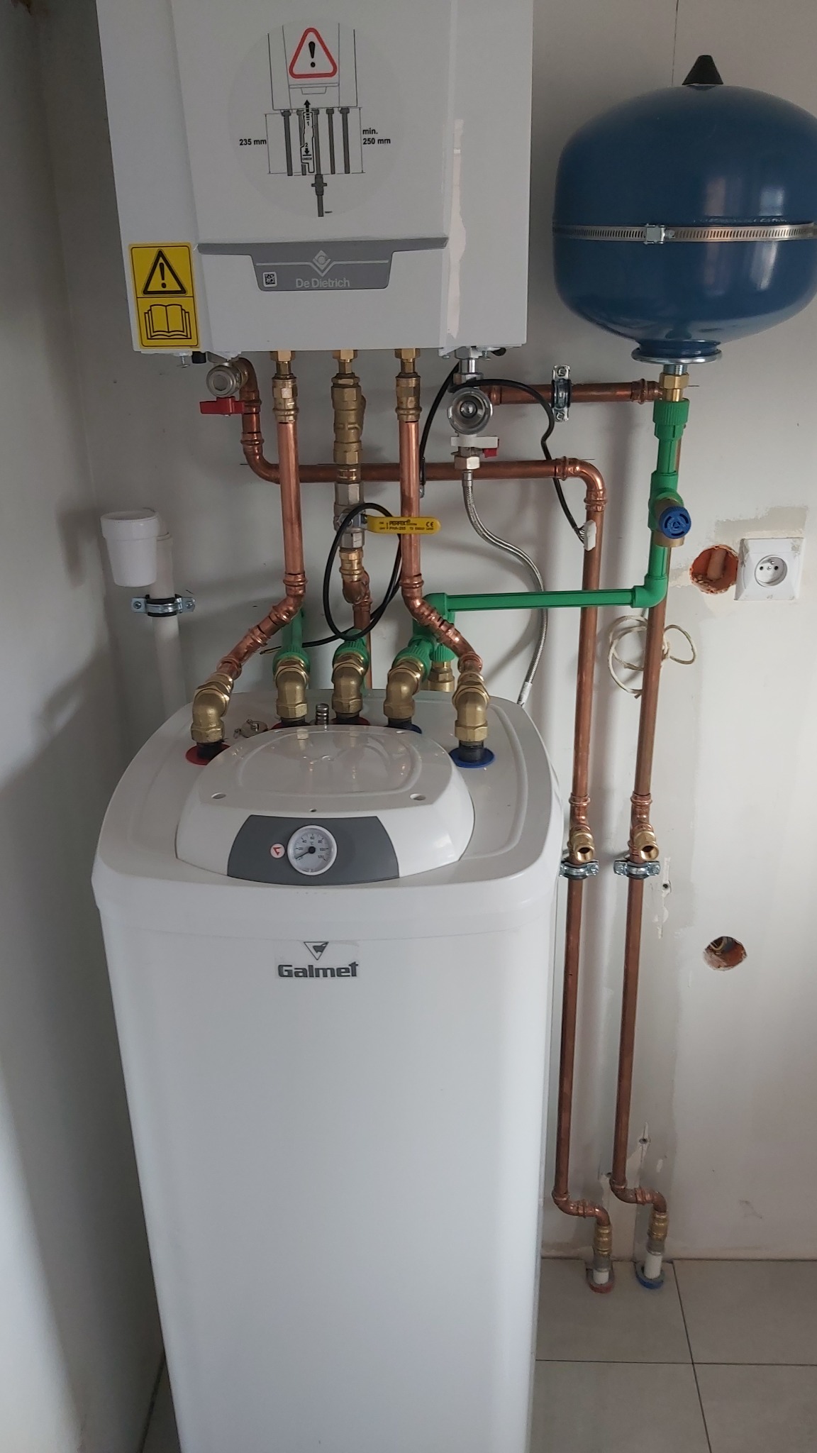 Zmontowany, wiszący piec gazowy De Dietrich z zasobnikiem Galmet i instalacją z miedzianych rur. Widoczne zawory, manometr i niebieski zbiornik wyrównawczy.