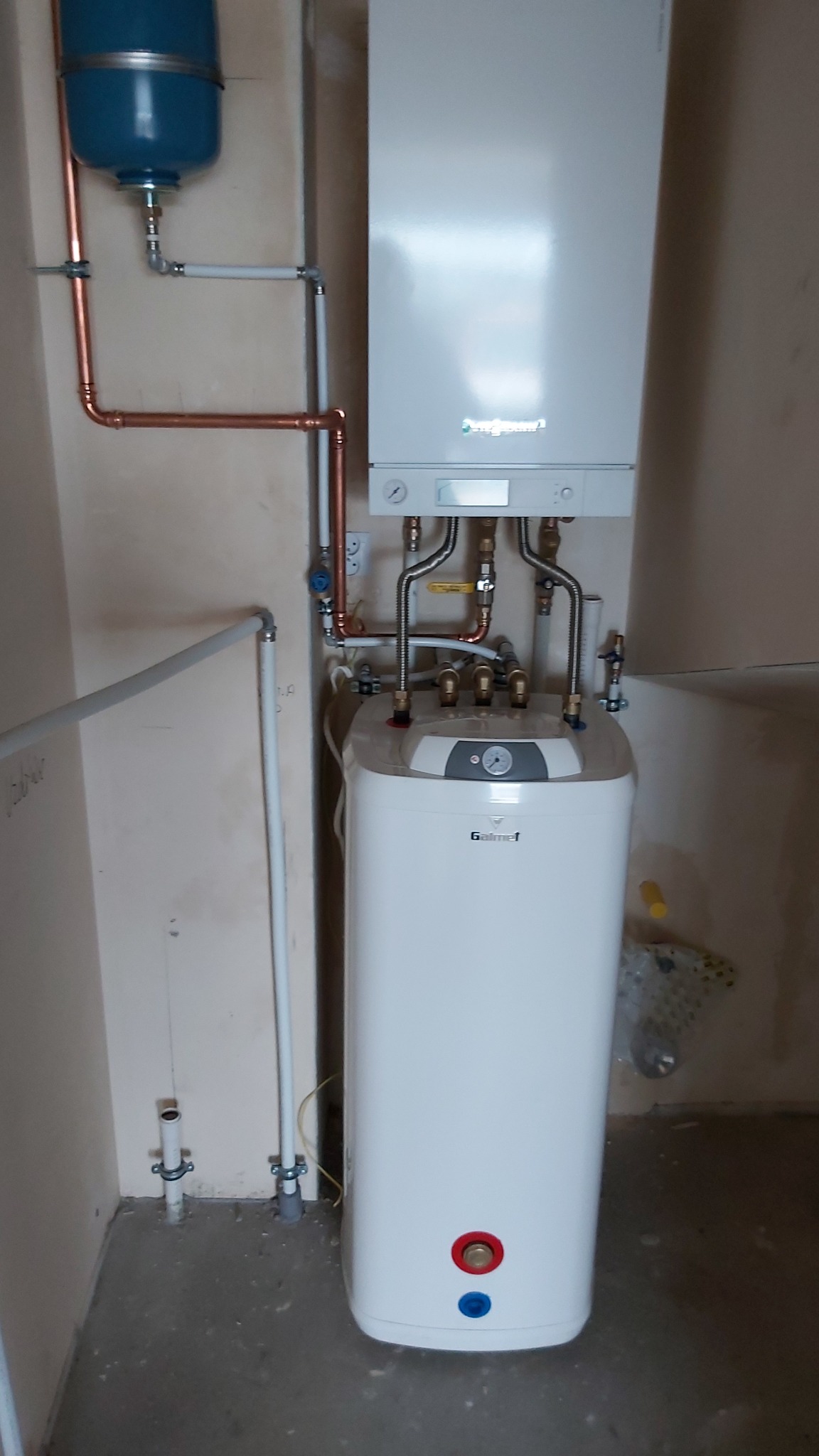 Biały piec gazowy Viessmann i zasobnik Galmet z miedzianymi rurami w nowym pomieszczeniu. Widoczne przyłącza i elementy instalacji grzewczej.