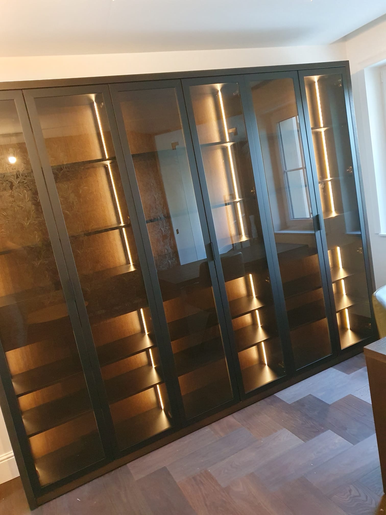 Nowoczesna, podświetlana szafa wnękowa z ciemnymi ramami i szklanymi drzwiami, widoczna na tle parkietu w Dobrodzieniu. Eleganckie wykończenie wnętrza.