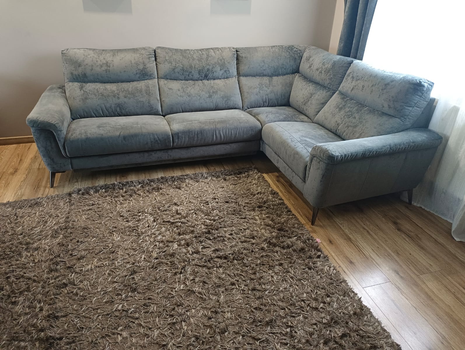 Szary, welurowy narożnik z brązowym dywanem shaggy na drewnianej podłodze. Nowoczesny design, miękkie oświetlenie, widok z niskiego kąta.