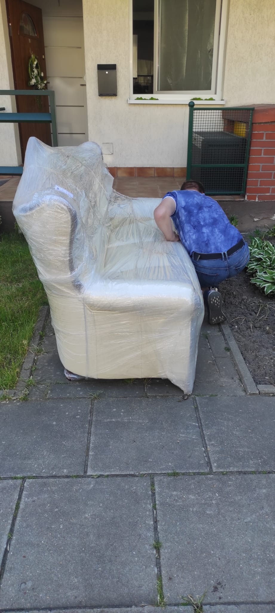 Sofa owinięta folią stretch, przygotowana do transportu w Dobrodzieniu. Pracownik firmy transportowej zabezpiecza mebel przed załadunkiem.