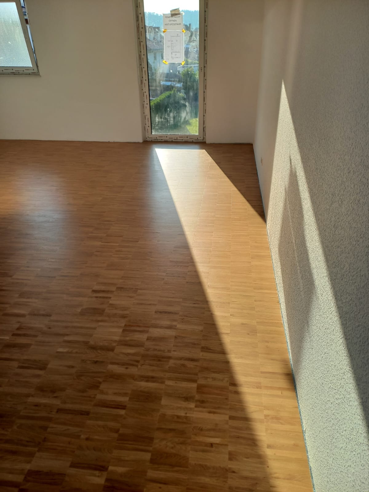 Jasny parkiet w jodełkę, zalany popołudniowym słońcem w pustym pokoju z oknem. Świeżo położona podłoga w nowym domu.