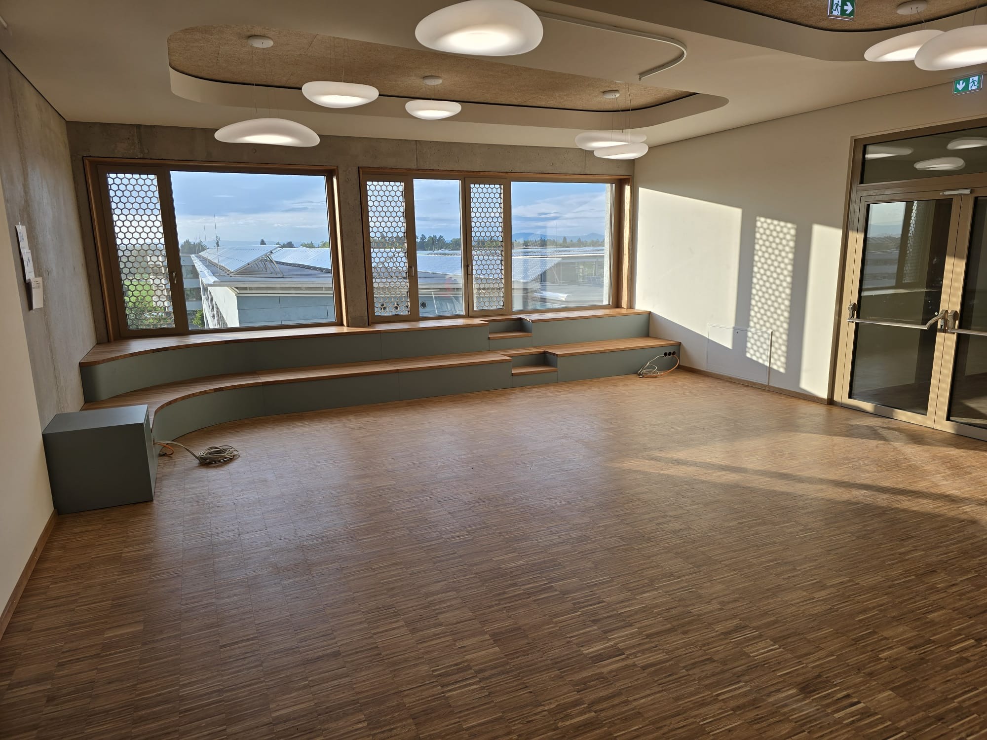 Parkiet w jodełkę francuską w jasnym, nowoczesnym wnętrzu z dużymi oknami i siedziskami. Widoczne detale wykończenia i oświetlenie.