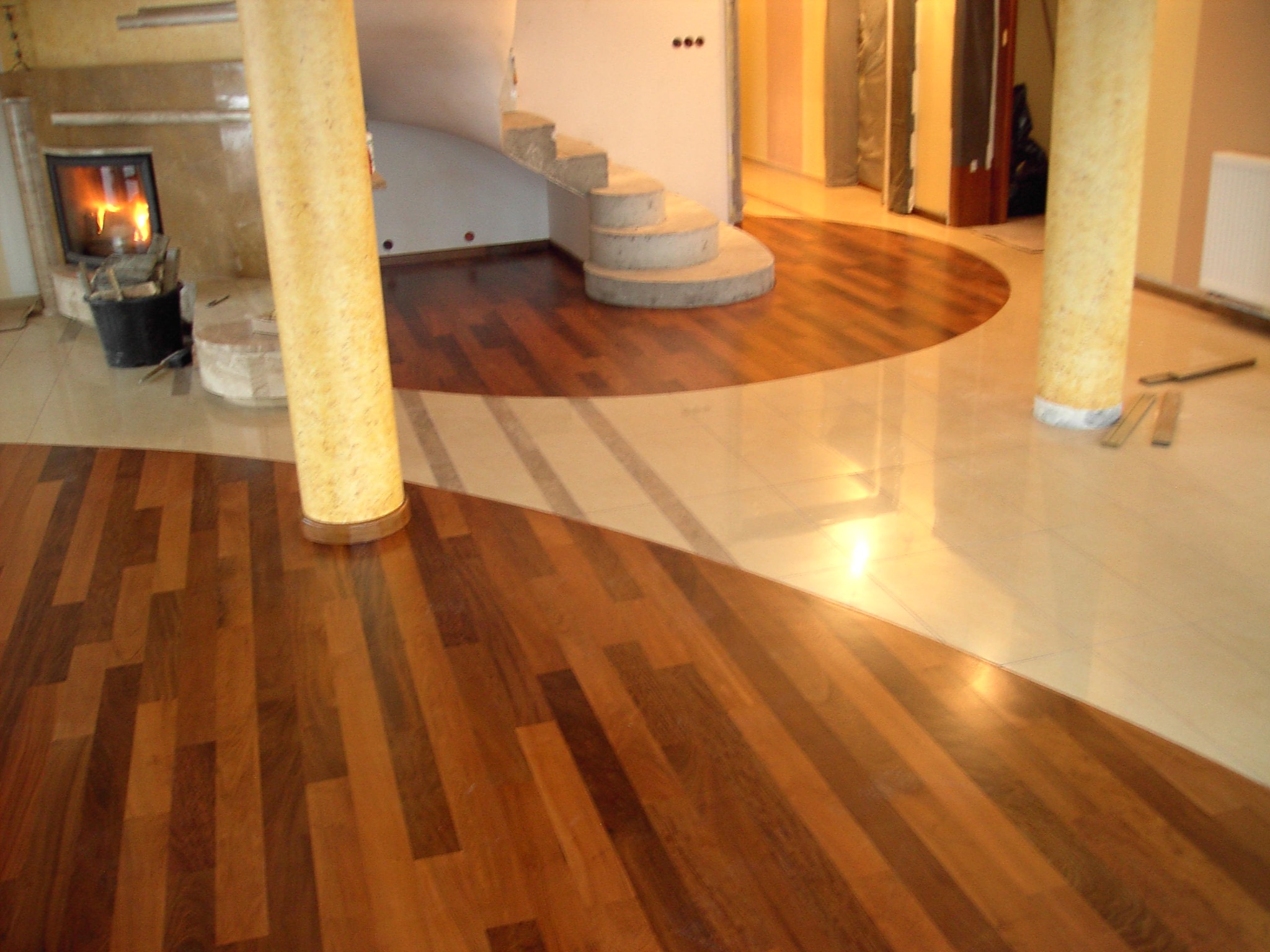 Parkiet w dwóch odcieniach drewna, ułożony w geometryczny wzór, z kolumnami i kominkiem w tle. Podłoga po renowacji, z połyskiem.