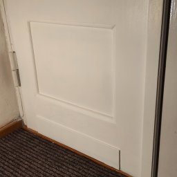 Perfect Walls Adam Andruch - Białe, odświeżone drzwi po malowaniu w Gorzowie Wielkopolskim. Widoczne zawiasy i fragment brązowej wycieraczki. Detal wykończenia wnętrza.