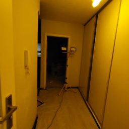 Perfect Walls Adam Andruch - Korytarz w trakcie prac przygotowawczych: podłoga zabezpieczona folią, widoczny statyw oświetleniowy. Ściany przygotowane do malowania.