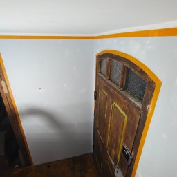 Perfect Walls Adam Andruch - Ściana po szpachlowaniu i zabezpieczeniu taśmą malarską przed malowaniem, widoczna stara drewniana futryna drzwiowa i ościeżnica. Przygotowanie do malowania.