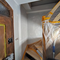 Perfect Walls Adam Andruch - Schody i ściana po szpachlowaniu, zabezpieczone folią i taśmą malarską. Widoczna stara, drewniana futryna drzwi. Przygotowanie do malowania.