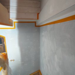 Perfect Walls Adam Andruch - Ściana po szpachlowaniu, zabezpieczona taśmą malarską, przygotowana do malowania w pomieszczeniu z drewnianym sufitem i schodami.