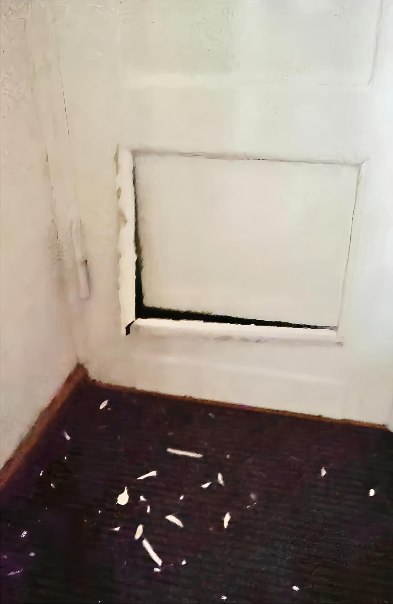 Narożnik pokoju z otworem w ścianie, przygotowanym do montażu okna lub drzwi. Widoczne ślady po usunięciu starej futryny i resztki gruzu na podłodze.