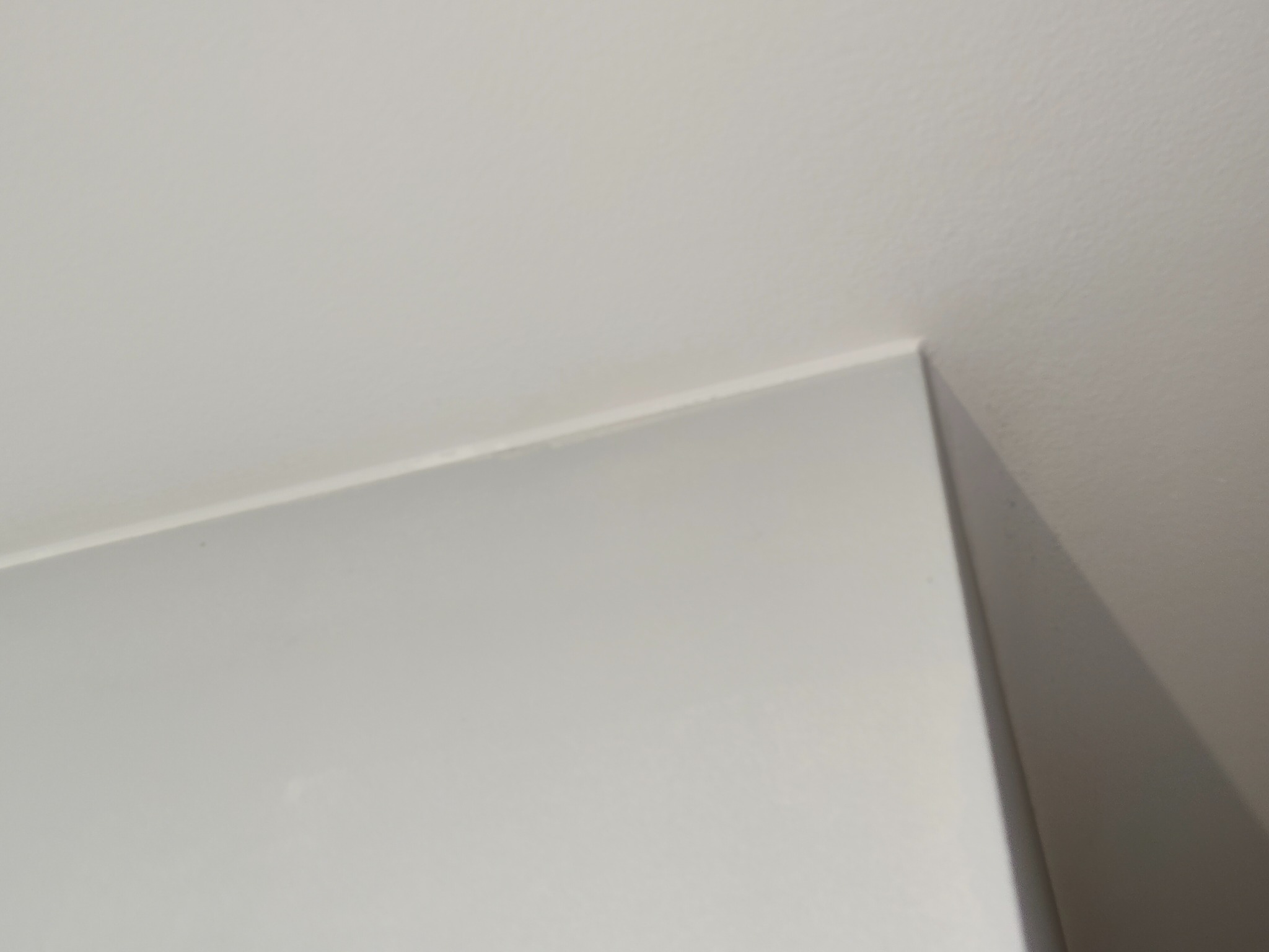 Biały róg pokoju, gdzie ściana łączy się z sufitem. Minimalistyczne ujęcie detalu wykończenia wnętrza, ukazujące precyzję łączenia powierzchni.