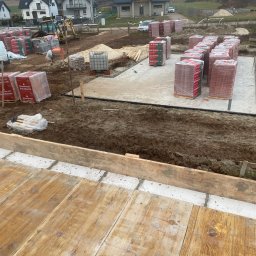 Usługi Remontowo Budowlane Dawid Szczepaniak - Fundamenty domu jednorodzinnego w trakcie budowy. Widoczne bloczki Porotherm, wykop, szalunki i przygotowany teren pod dalsze prace. W tle zabudowa mieszkalna.