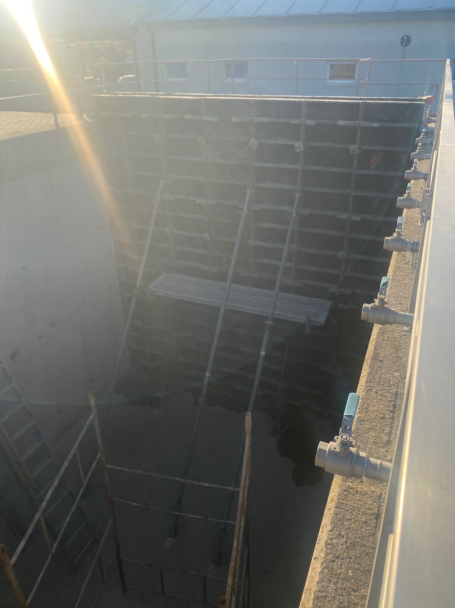 Wnętrze betonowego zbiornika w trakcie budowy, widoczne szalunki, drabiny i instalacje. Słoneczne światło podkreśla surowość konstrukcji.