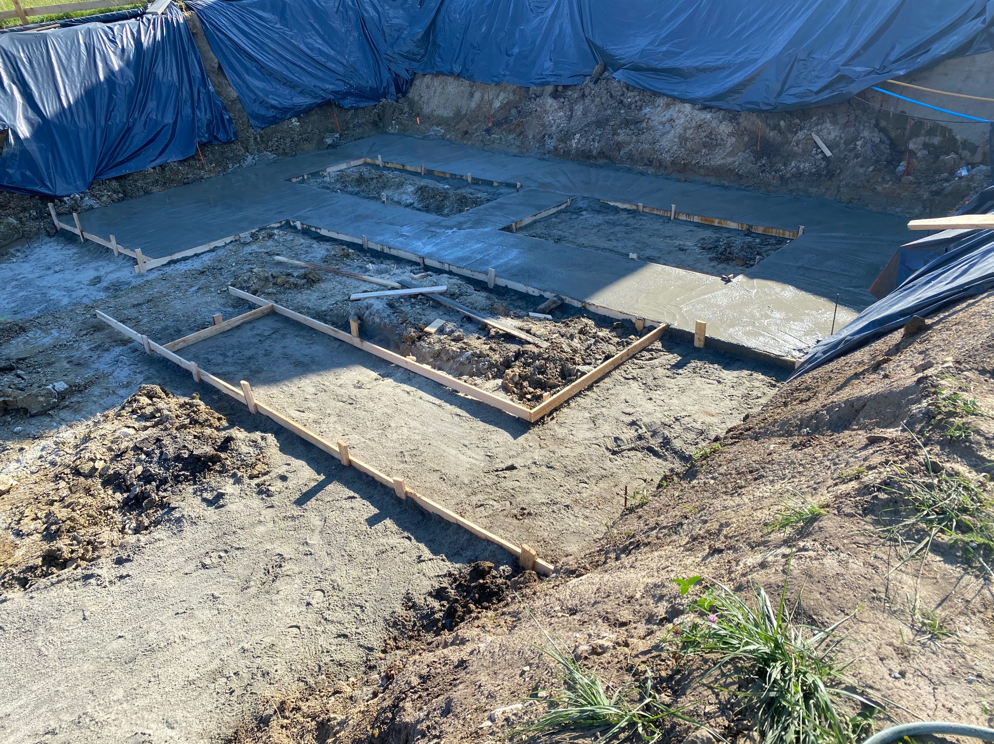 Wylany fundament pod budowę domu z drewnianymi szalunkami. Wykop zabezpieczony folią. Widok z góry na plac budowy w słoneczny dzień.