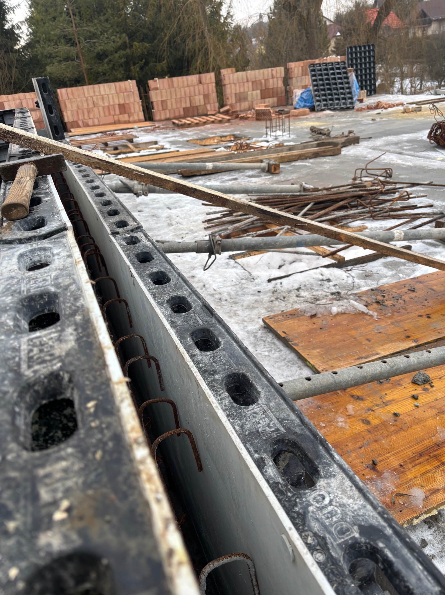 Szczegółowe ujęcie szalunku fundamentowego z widocznym zbrojeniem, przygotowanego do zalania betonem na placu budowy w zimowych warunkach.