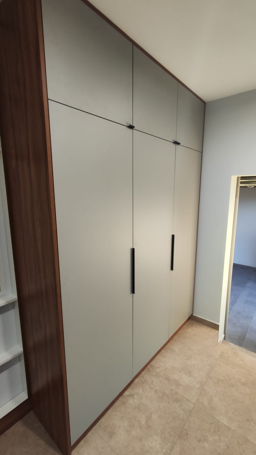 Szara szafa wnękowa z ciemnymi uchwytami, dopasowana do wnętrza w Dębnie. Obudowa z ciemnego drewna, jasna podłoga, widok na korytarz.