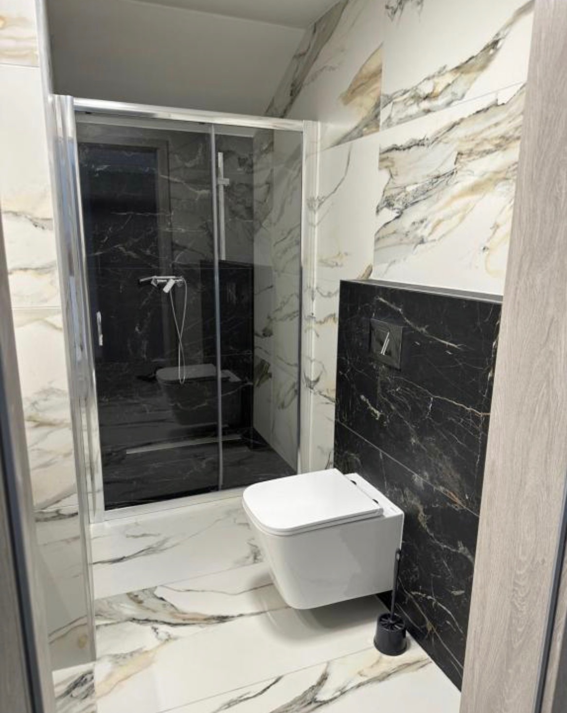 Nowoczesna łazienka z kabiną prysznicową i podwieszaną toaletą. Marmurowe płytki w odcieniach bieli i czerni. Minimalistyczny design, eleganckie wykończenie.