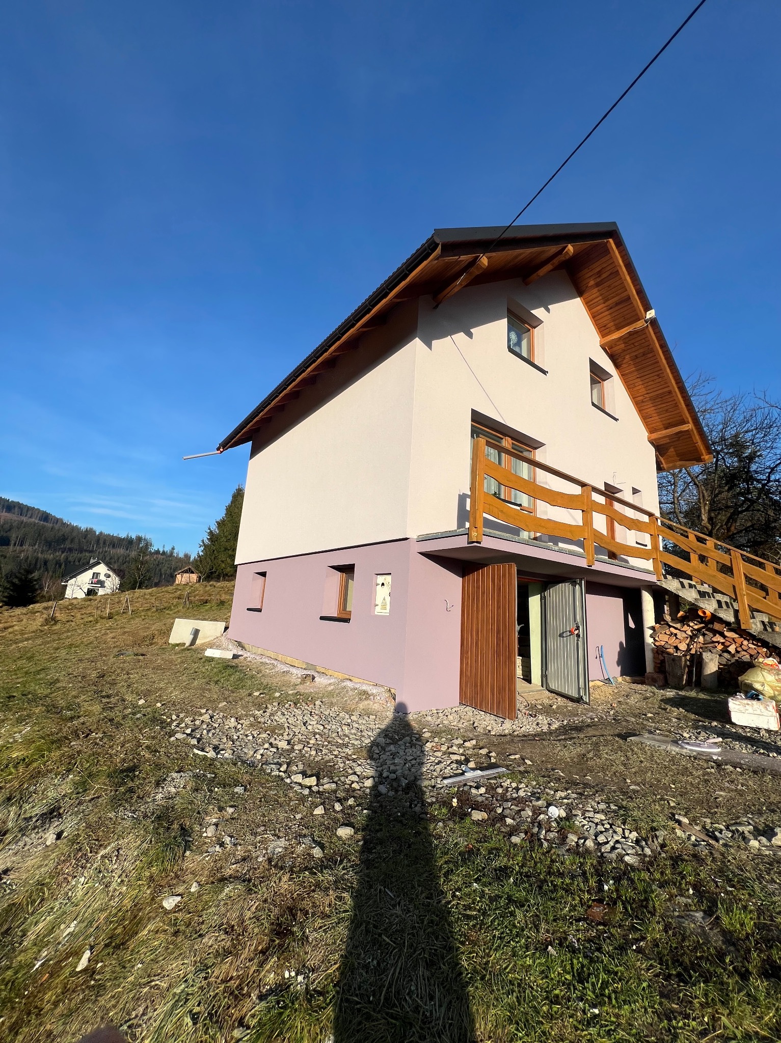 Dwukondygnacyjny dom z drewnianą balustradą w Wiśle, świeżo pomalowany na beżowo i fioletowo, z otwartymi drzwiami do piwnicy i stosem drewna obok.