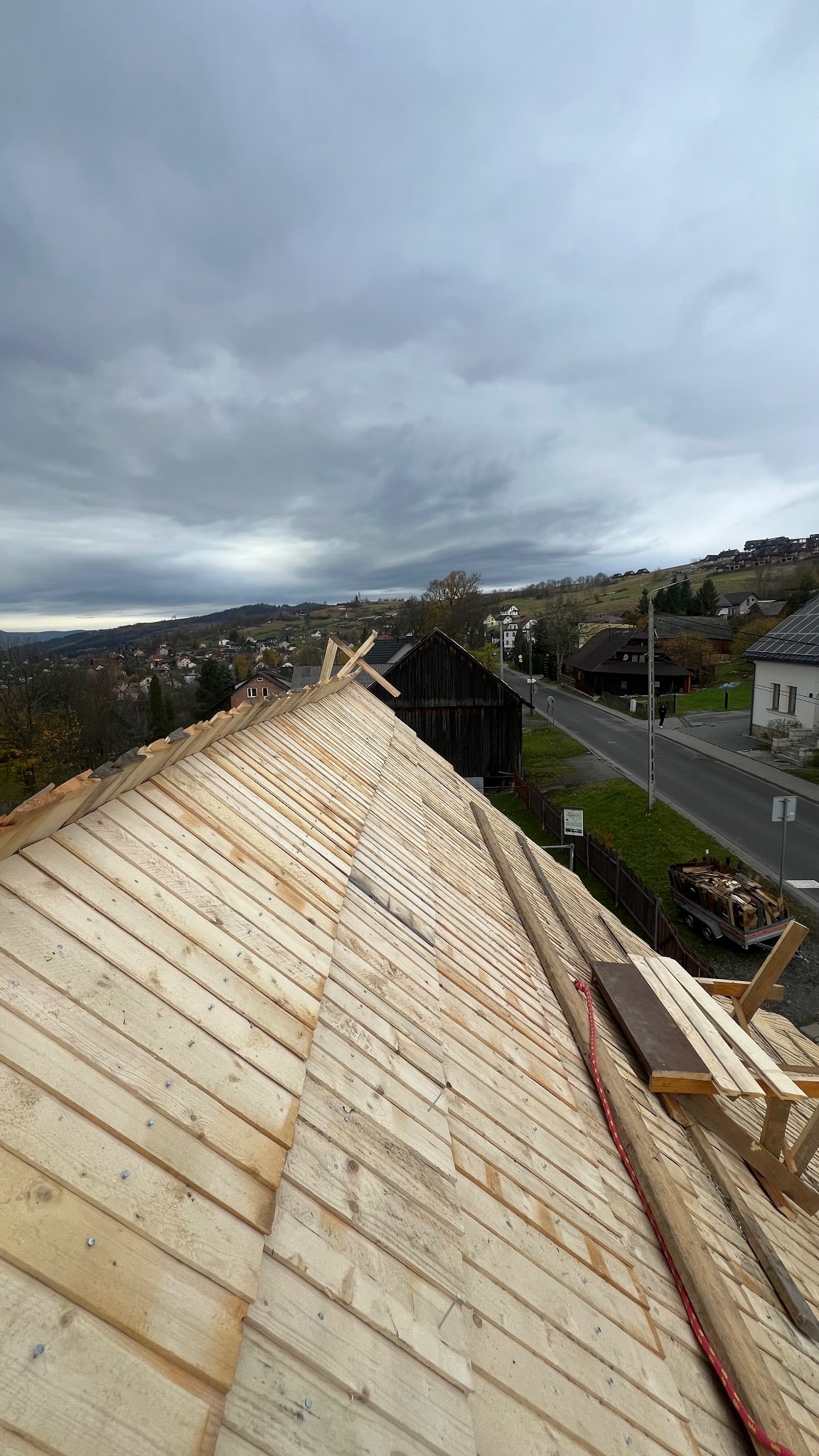 Konstrukcja dachu z desek w trakcie budowy, widok z góry na tle zabudowań i pochmurnego nieba. Widoczne elementy mocujące i narzędzia.