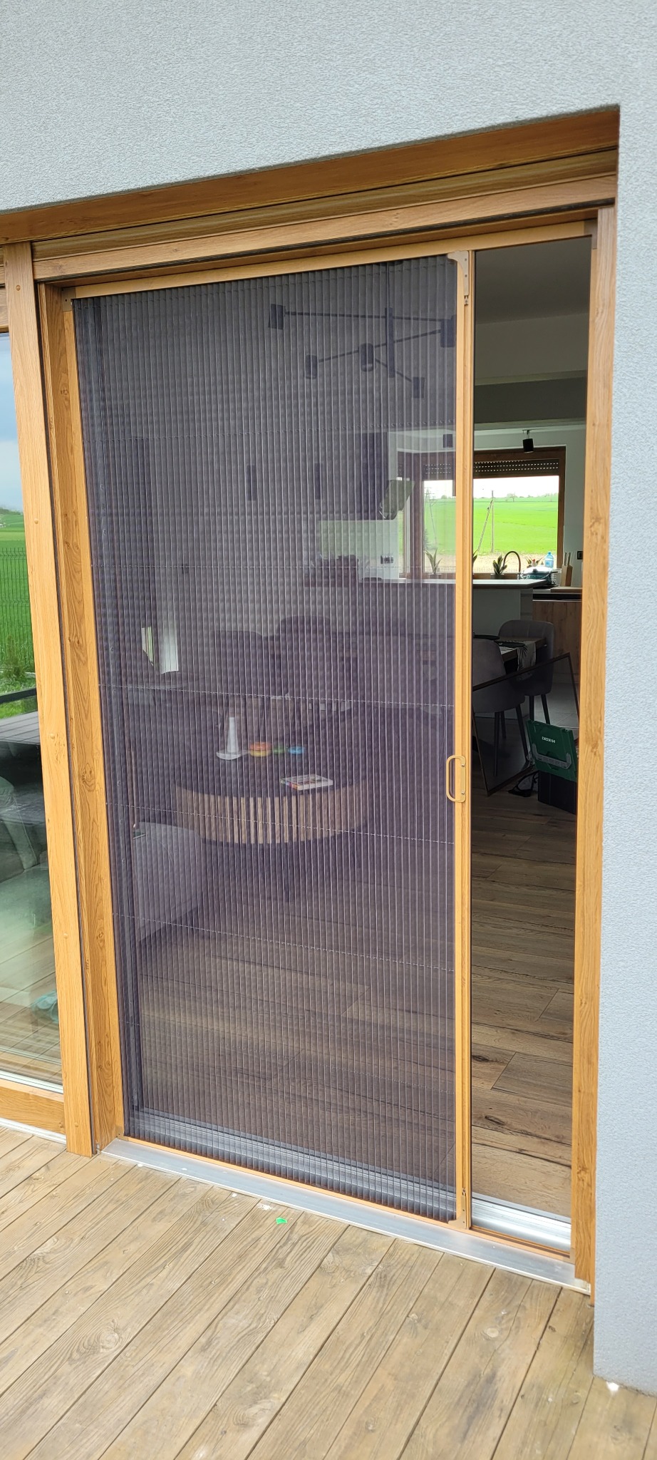 Zewnętrzna moskitiera plisowana w drewnianej ramie, zamontowana na tarasie. Widok na wnętrze domu przez siatkę. Nowoczesne rozwiązanie na owady.