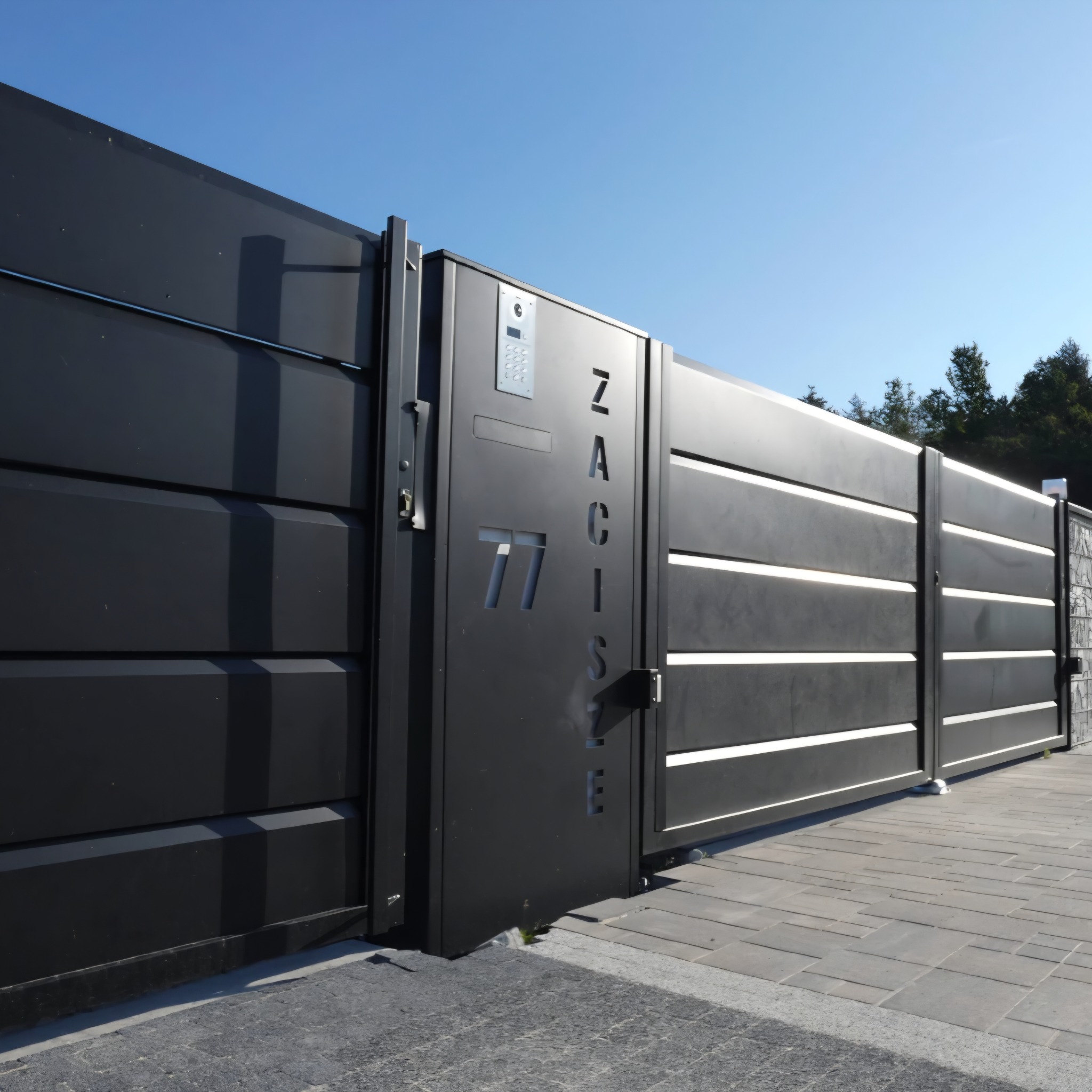 Nowoczesna, przesuwna brama wjazdowa w kolorze antracytu z numerem domu '77' i nazwą 'ZACISZE' wyciętymi laserowo. Brama z interkomem, na tle błękitnego nieba.