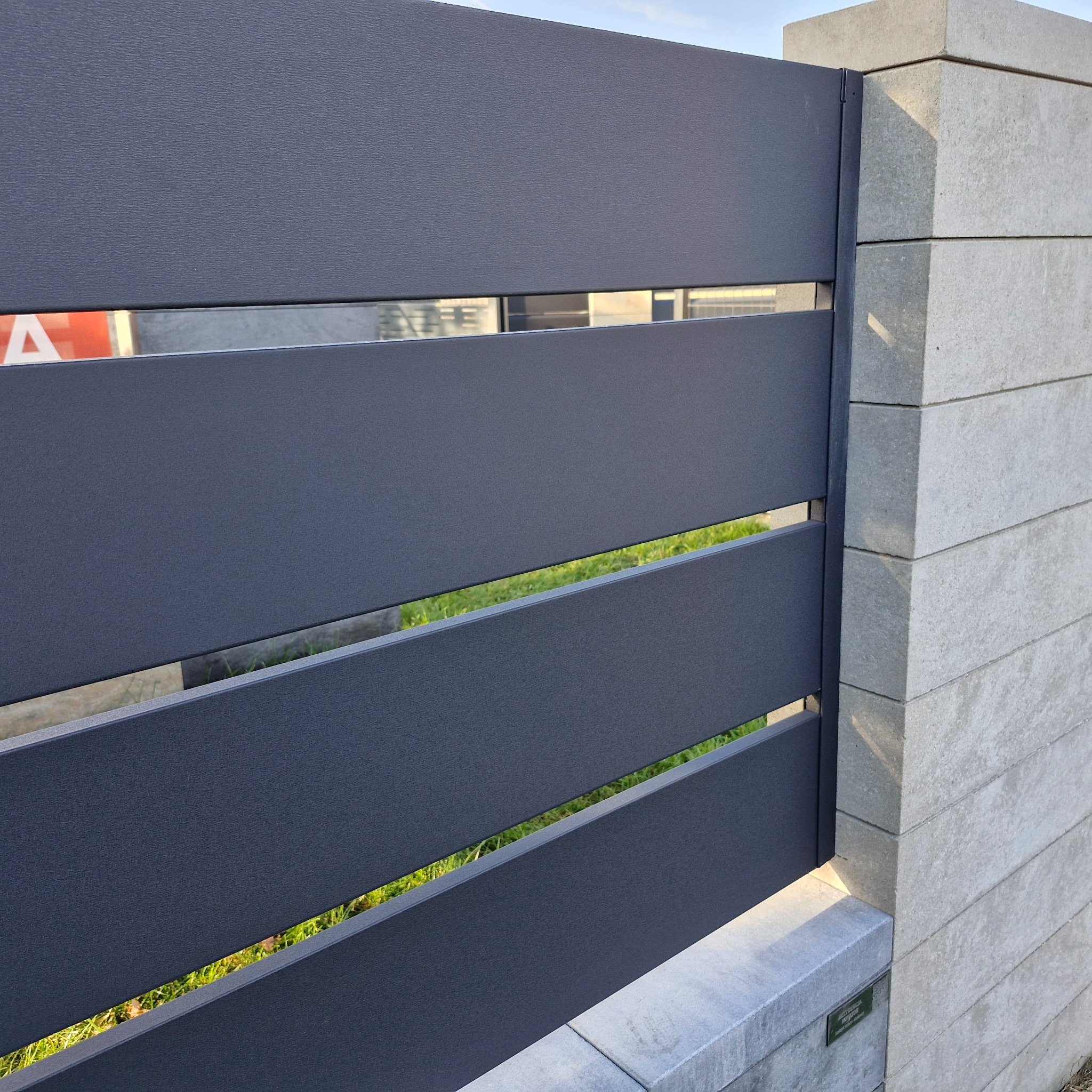 Nowoczesne, grafitowe ogrodzenie metalowe z poziomymi panelami i betonowymi słupkami. Widok z bliska, ukazujący detale konstrukcji i fakturę materiałów.