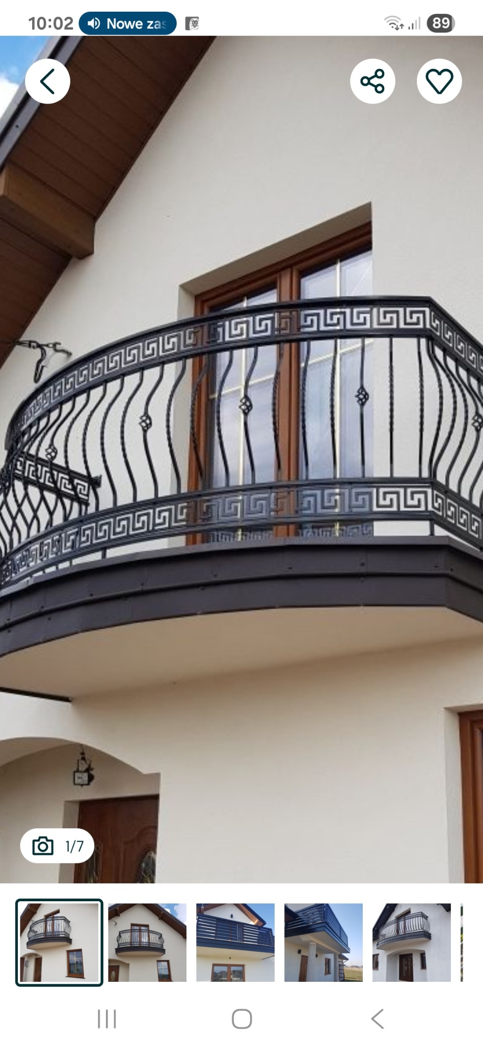 Elegancka, czarna balustrada balkonowa z motywem greckim, zamontowana na balkonie domu z jasną elewacją. Widok z dołu, podkreślający detale i kształt balustrady.